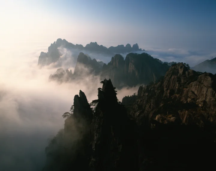 云雾缭绕的险峻山峰与松树构成宁静壮丽的自然景观。