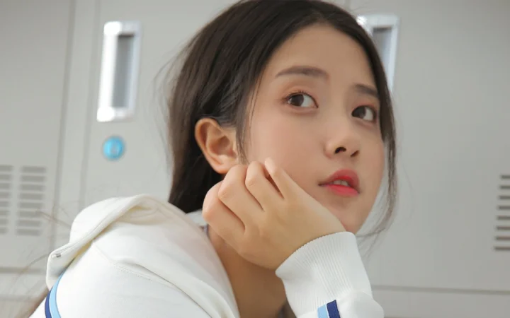 一位成年女性身穿白色连帽衫，手扶脸颊看向镜头。