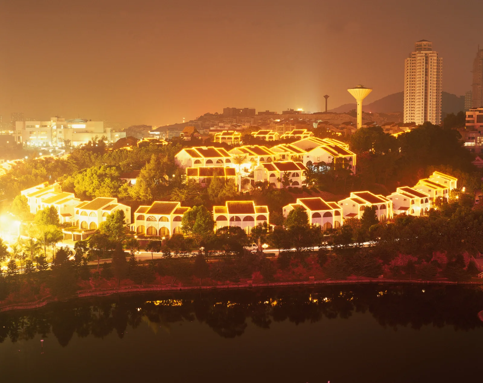 夜色中的城市建筑和明亮灯光倒映在前方的湖面上。