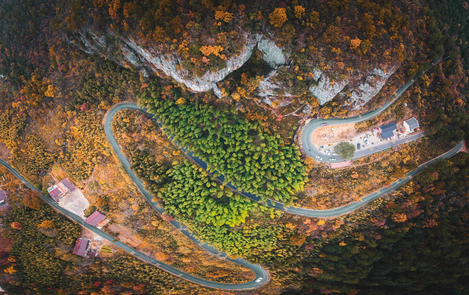 俯瞰视角展现了秋色山林、裸露岩壁和蜿蜒盘山公路。