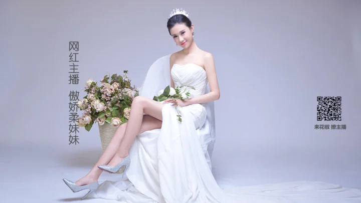 一名女子穿着白色礼服坐在浅灰色摄影棚背景前，手持一束花。