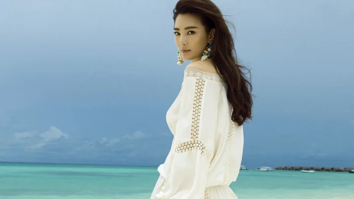 一位身穿白色长袖上衣的成年女性站在蓝色海水与天空前。