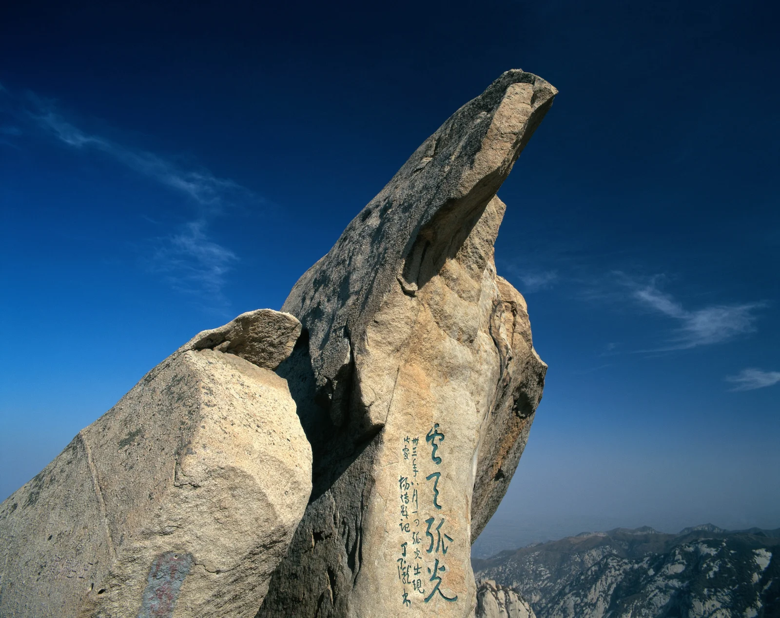 一座巨大的岩石山峰矗立在深蓝天空下，远处可见层叠山脉。