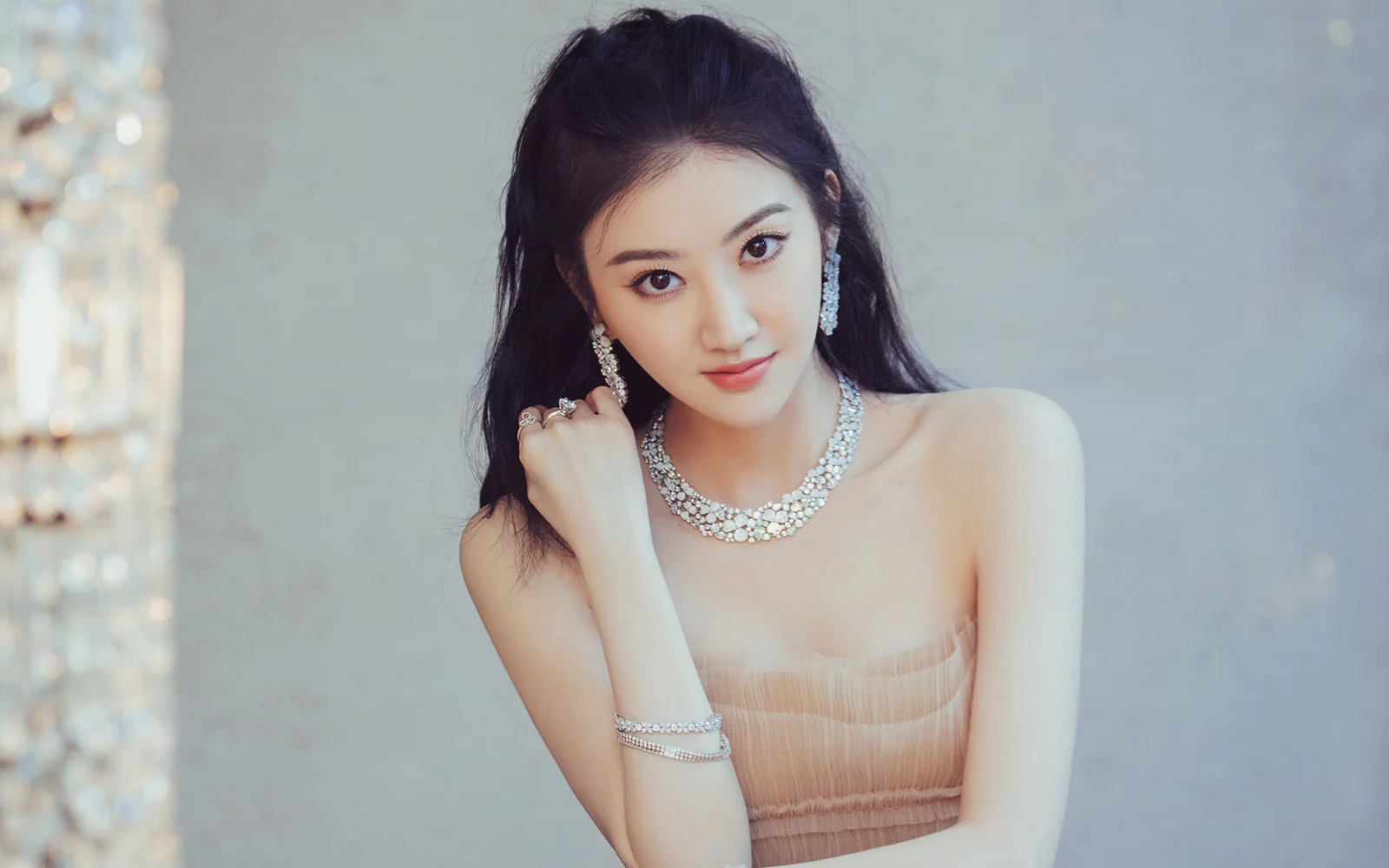 一位佩戴闪亮项链、耳饰和手链的女性在室内背景前面对镜头微笑。