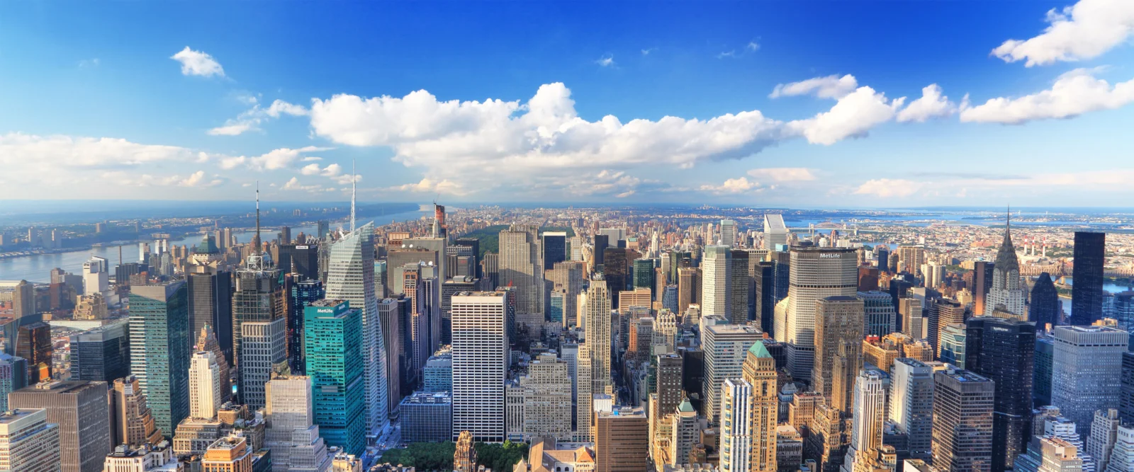青空の下、高層ビルが立ち並ぶ都市の skyline が遠くまで広がっている。