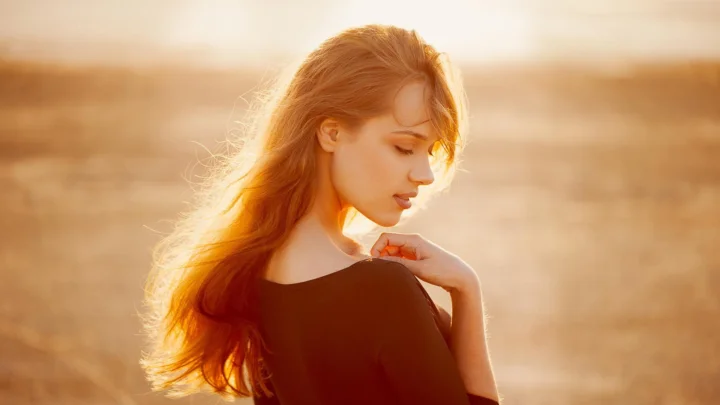 一名红发女子在温暖的夕阳光线中侧身回望。