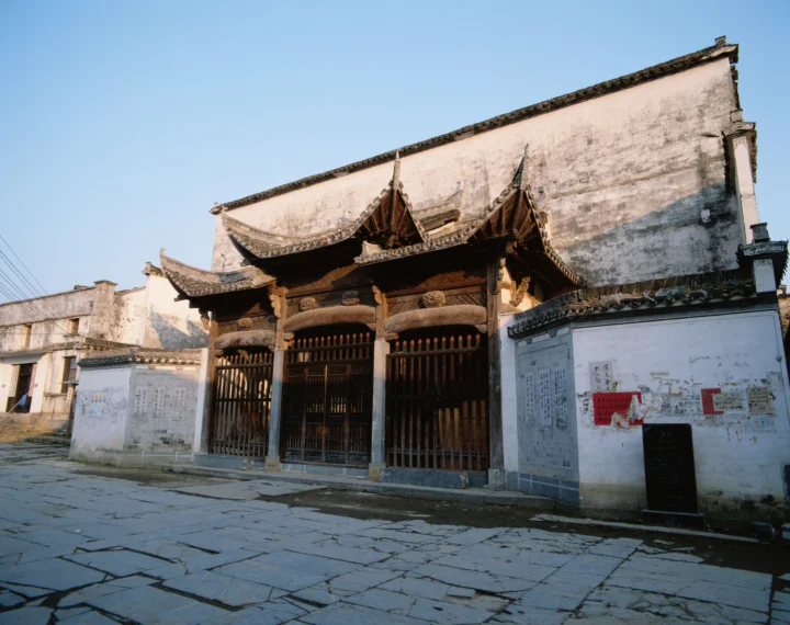 蓝天下，一座带有 ornate 木雕门楼的中国传统建筑临着石板街道而立。