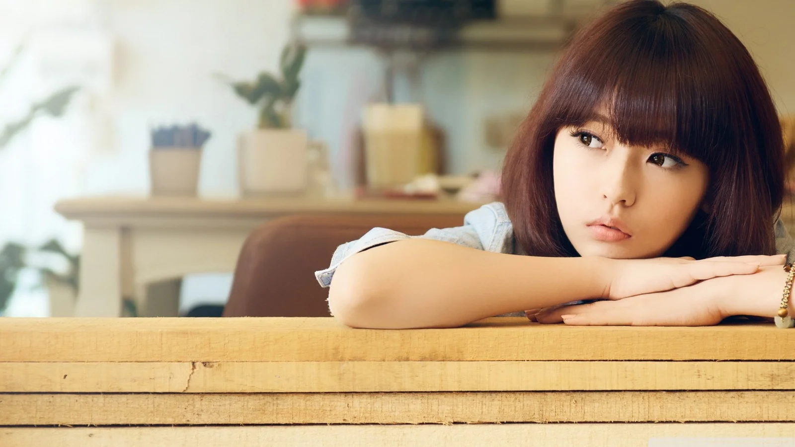 一名女性趴在木桌上，望向画面右侧，背景是明亮的室内空间。