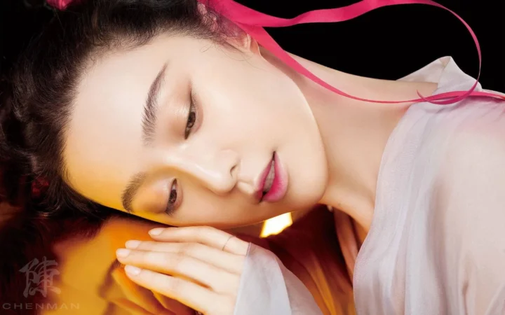 画面是一位成年女性的近距离侧脸肖像，她双手合拢，周围点缀着粉色丝带。