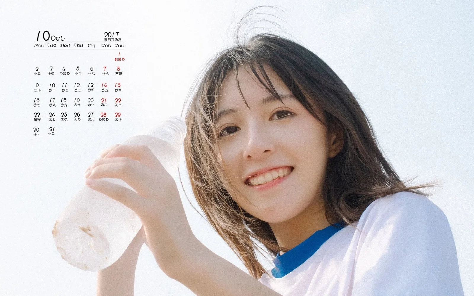 白と青の服を着た女性が明るい背景の前でカメラに向かって微笑んでいます。