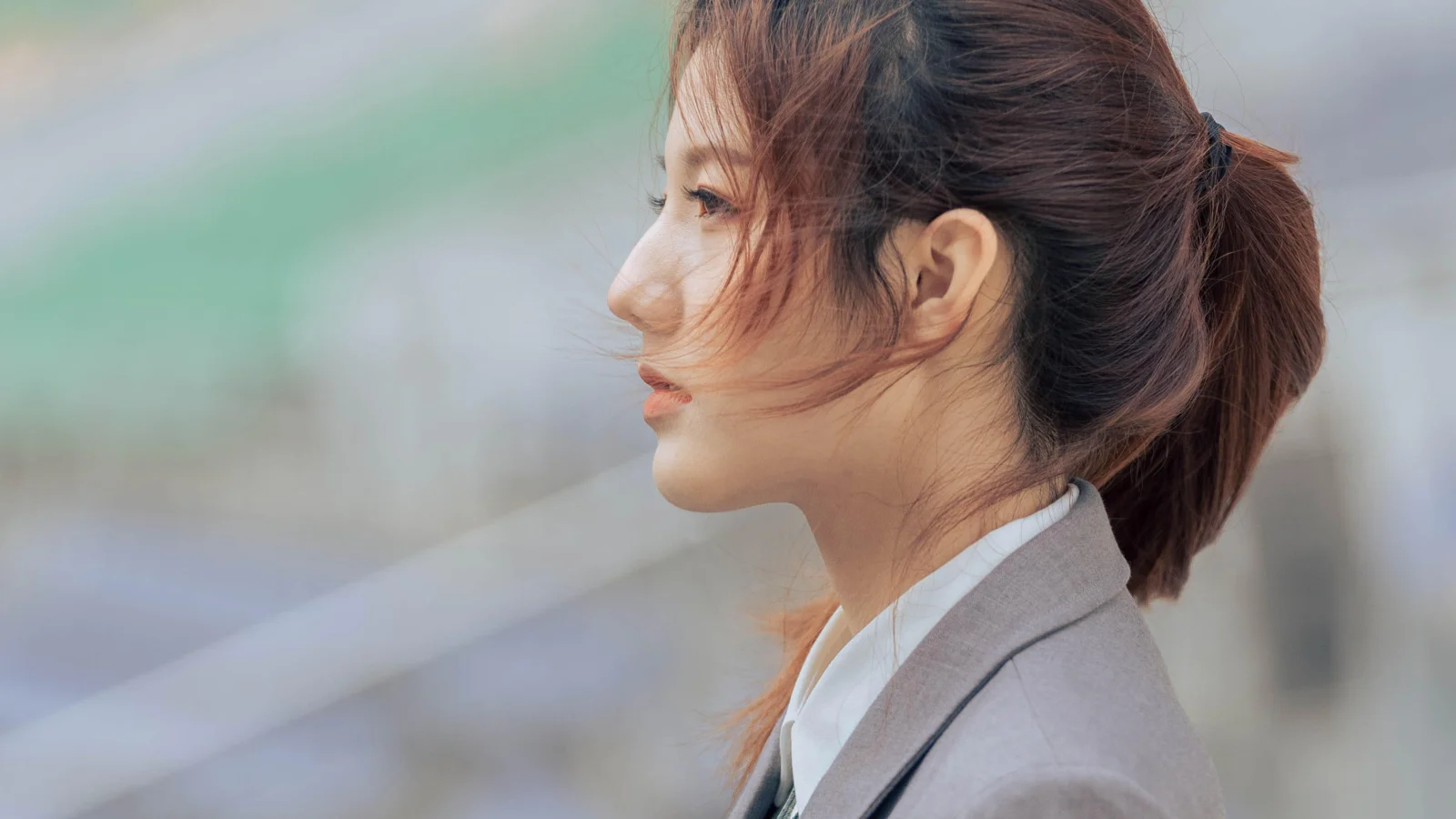 一位扎着马尾、身穿灰色西装外套的女性侧脸面对模糊背景。