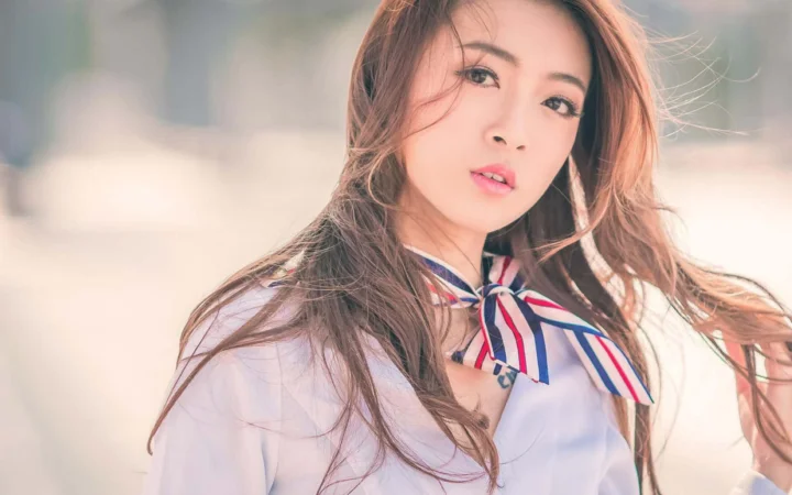 一名长发女性身穿带有彩色蝴蝶结的浅色上衣，面向镜头拍摄。