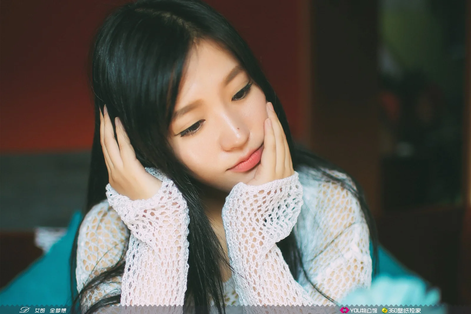 검은 머리의 여성이 두 손으로 뺨을 받치고 부드러운 표정을 짓고 있습니다.