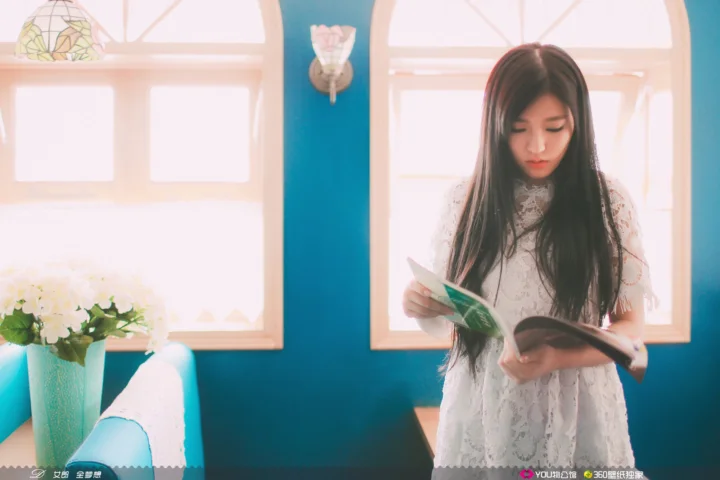 一名长发女子站在明亮的窗边阅读书籍。