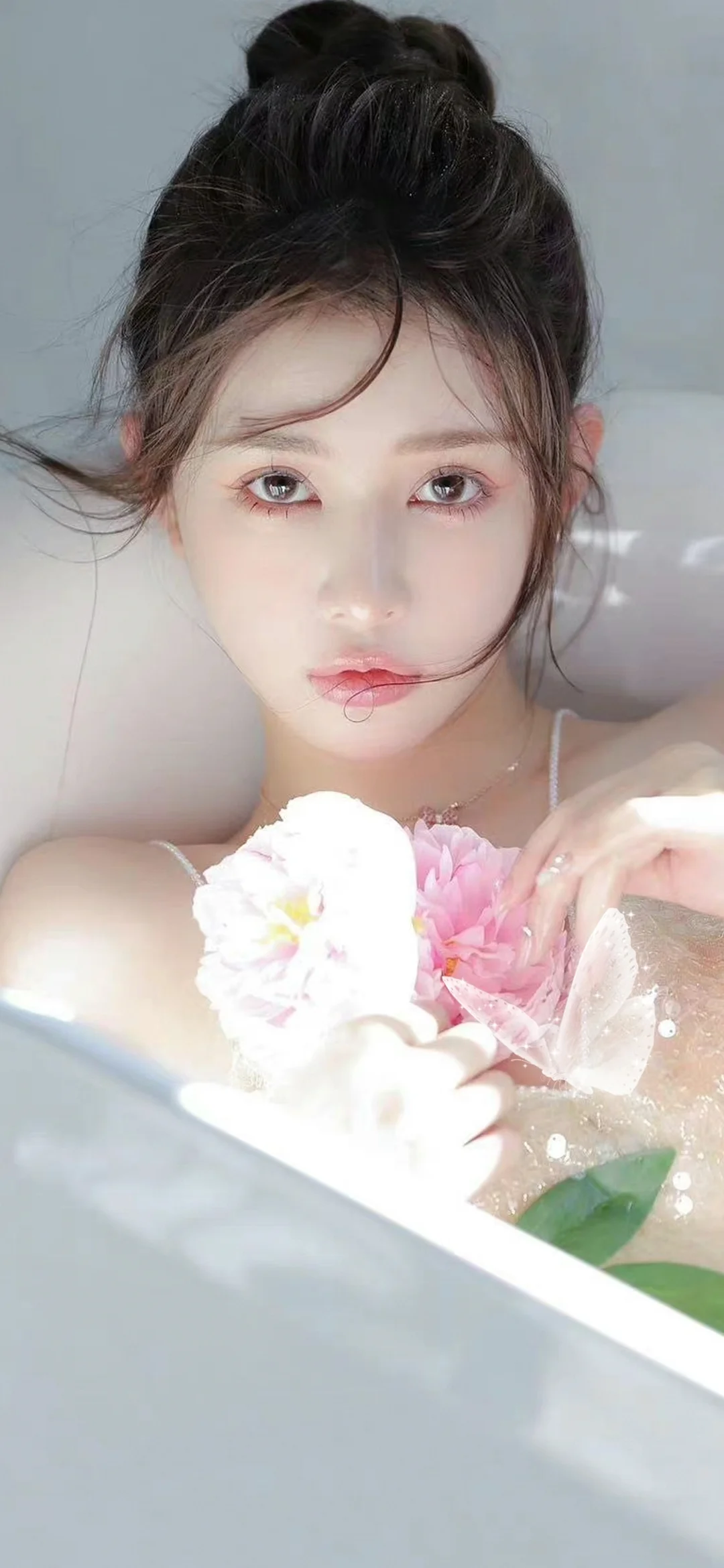 一位成年女性近距离面对镜头，手捧白色和粉色花束，背景为浅色墙面。
