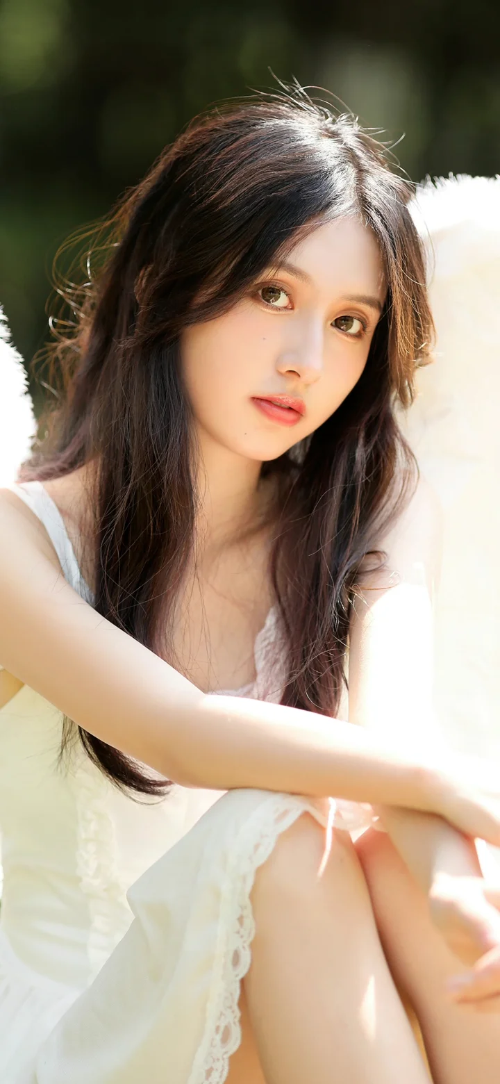 흰색 옷을 입은 긴 머리 여성이 부드러운 햇살 속에서 카메라를 바라보고 있다.