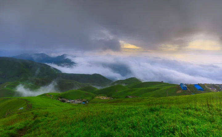 云雾缭绕的群山延伸在翠绿的草原上，远处的天空透出柔和的光线。