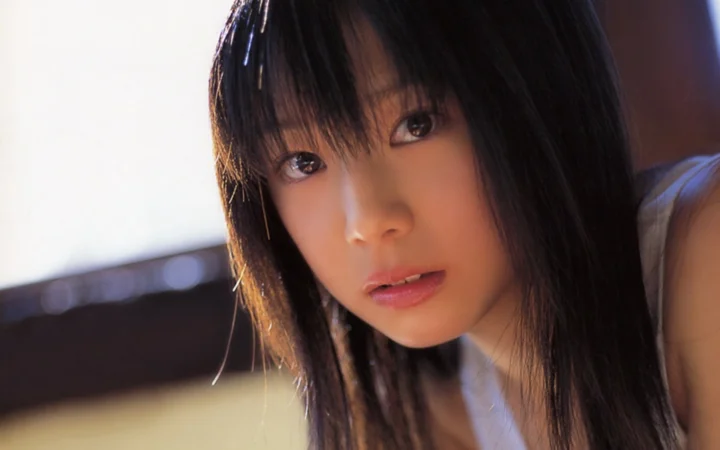 明るく柔らかな背景を前にした黒髪女性の顔のクローズアップポートレートです。