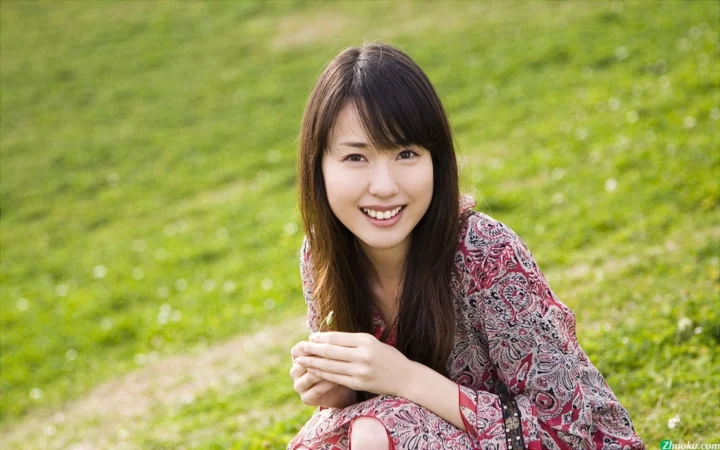 一名面带笑容的女子坐在户外绿草地上，身穿图案长袖服装。