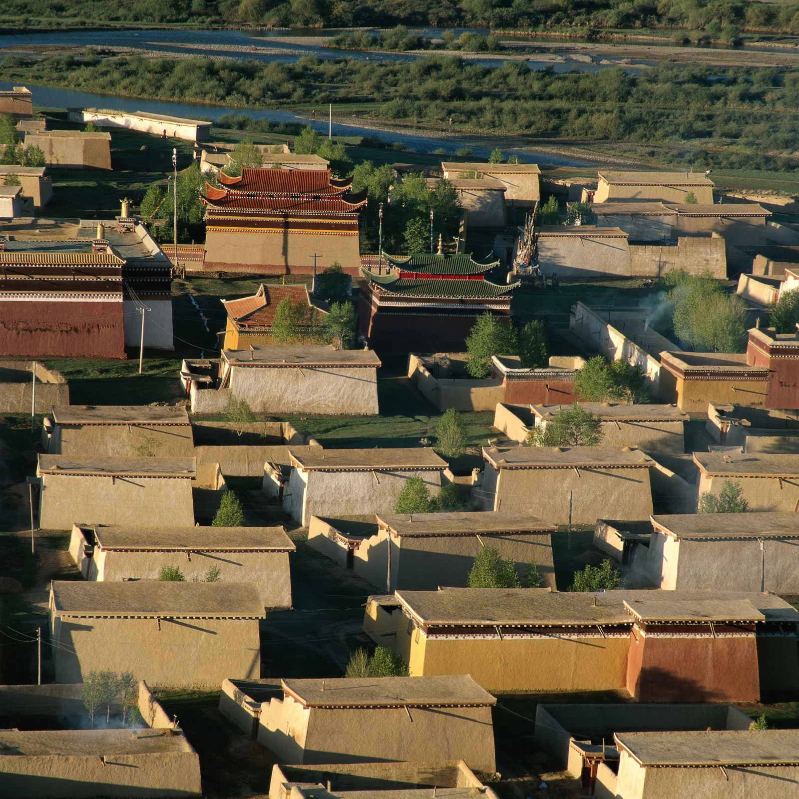 阳光照耀下的传统村落建筑依河而建，远处可见河流与绿地。