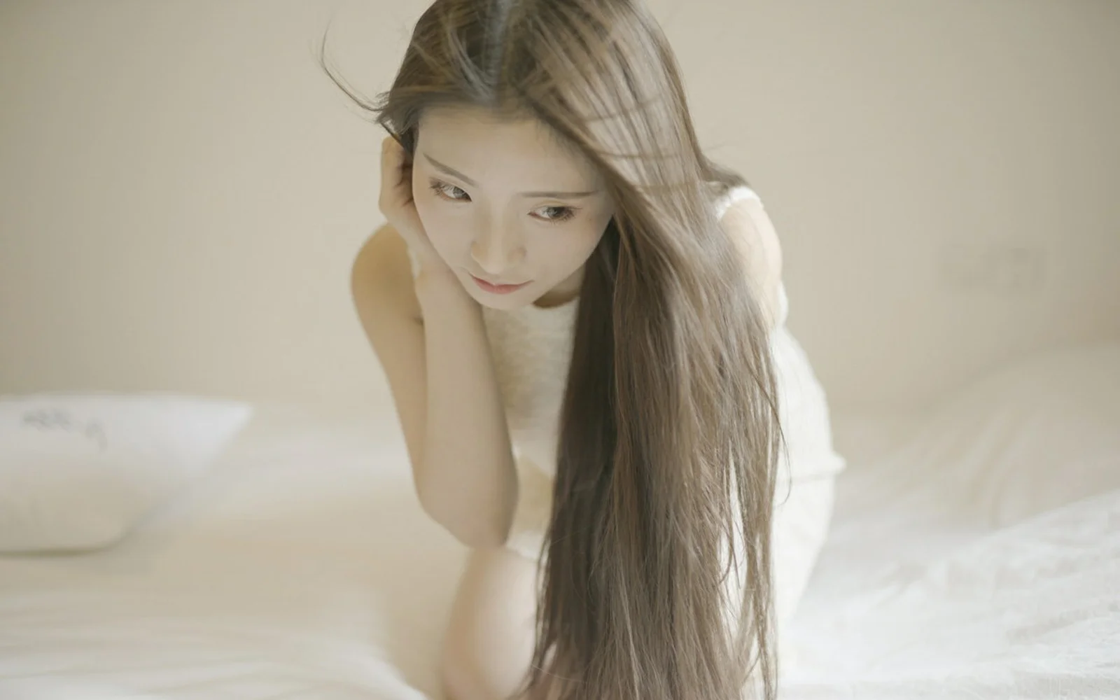 부드러운 빛 속에서 긴 머리의 여성이 침대 곁에 앉아 있습니다.