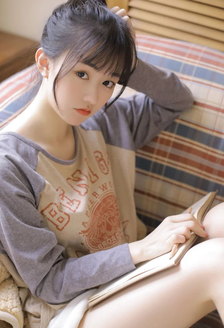 室内で女性がベッドのそばに座り、本を手に読んでいる。