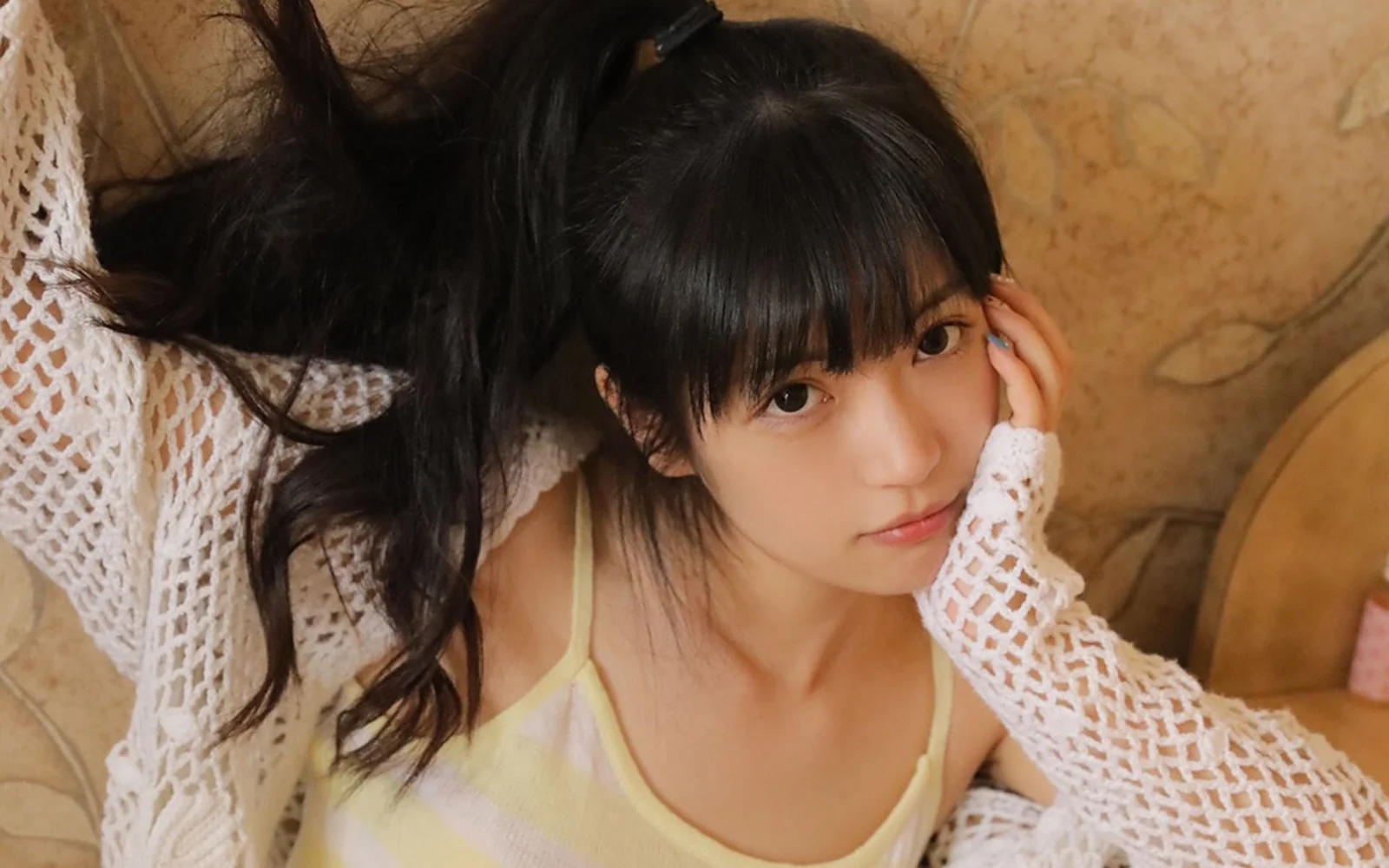 黒髪の女性が室内のソファに寄りかかり、カメラに向かって自然な表情を見せているポートレートです。
