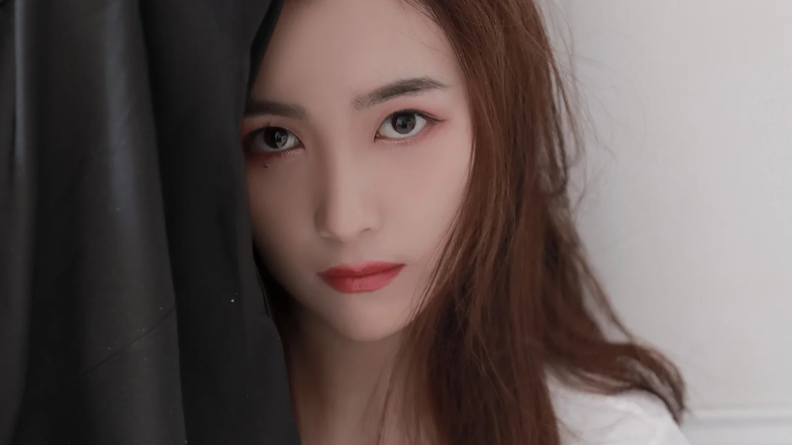 一名棕色长发女性的近距离肖像，脸部被黑色布料部分遮挡，背景为浅色。