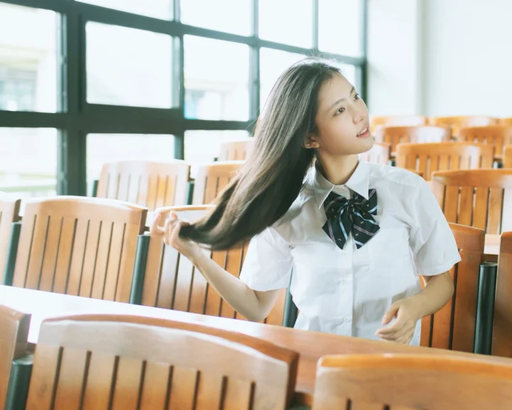 一名长发女性坐在明亮的教室里，轻轻拨动头发。
