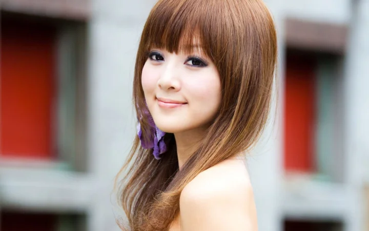 一位棕色长发女子面带微笑，背景是虚化的建筑立面。