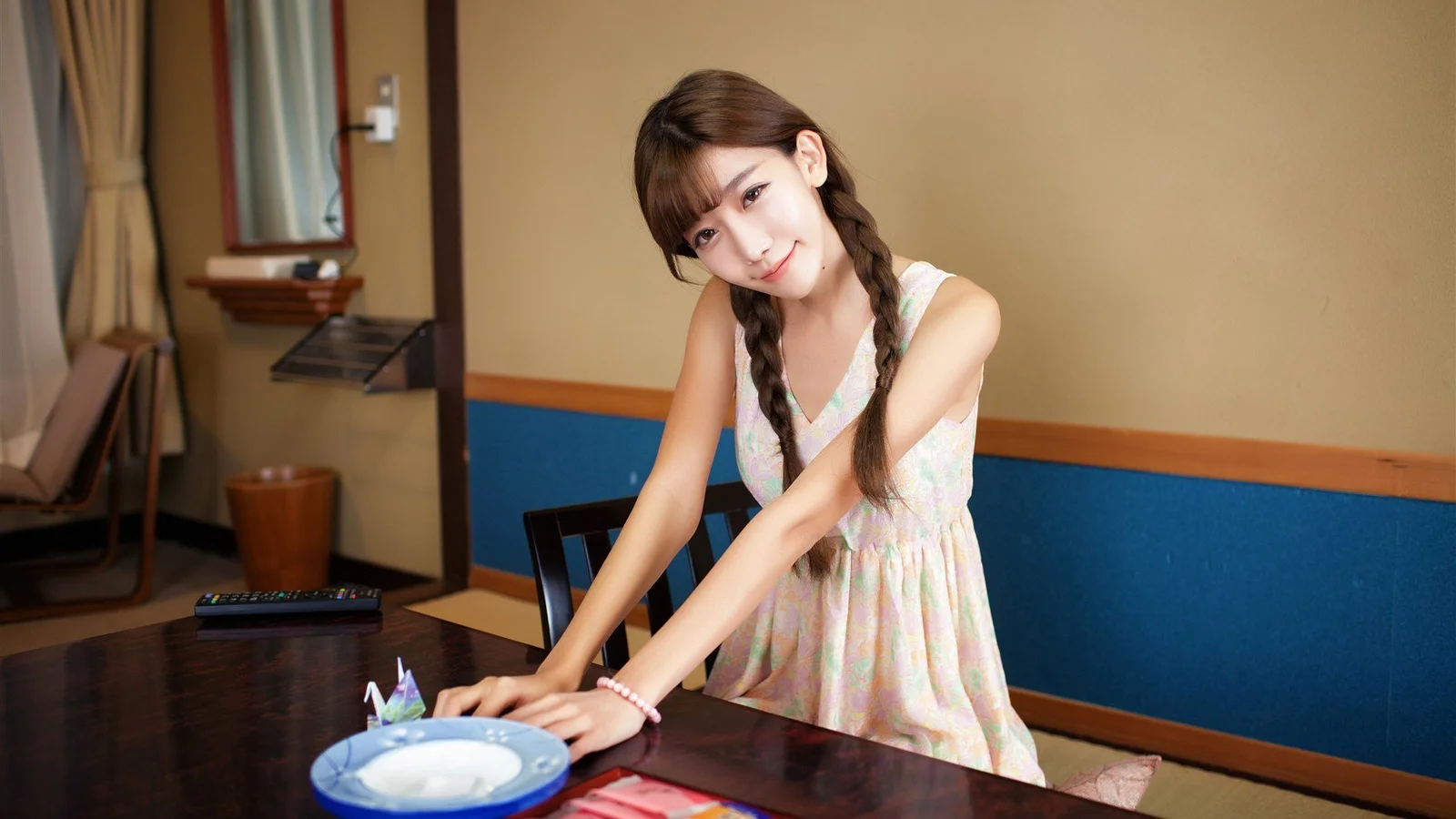 一名成年女性在室内餐桌旁俯身摆放餐具。