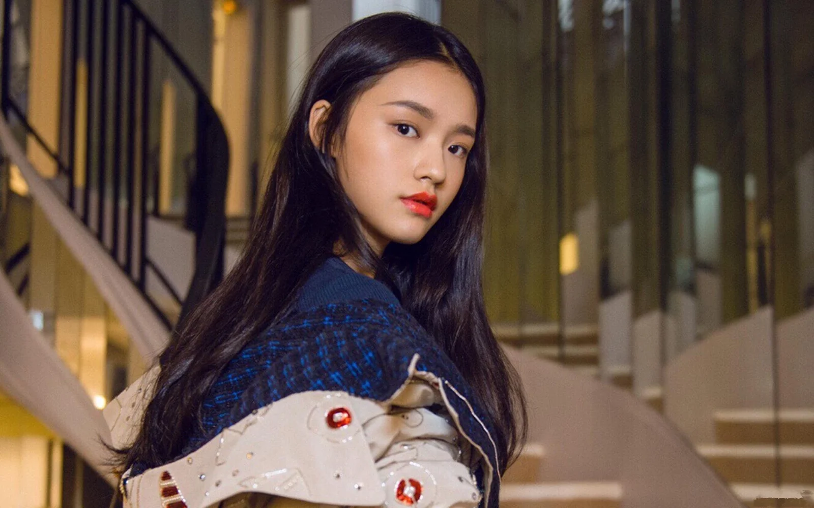 一名长发女性站在室内楼梯旁回头看向镜头。