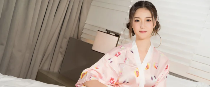 一位成年女性身穿粉色图案服装坐在室内窗帘与百叶窗前。