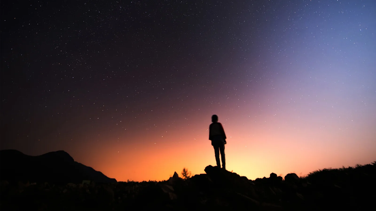 群山剪影前的地平线映着橙色日落，夜空中散布着星星。