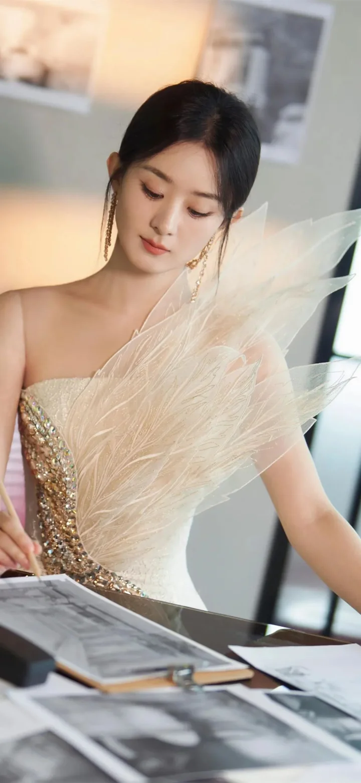 一名身穿浅色羽饰礼服的女性低头坐在键盘乐器旁，前方放着乐谱。