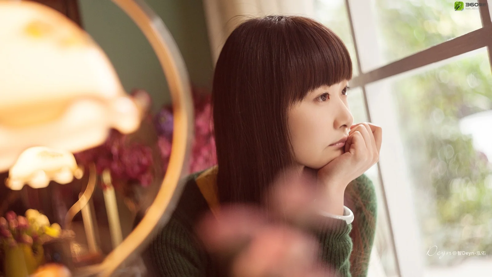 一名成年女子坐在窗边，暖色灯光和室内景物构成柔和画面。