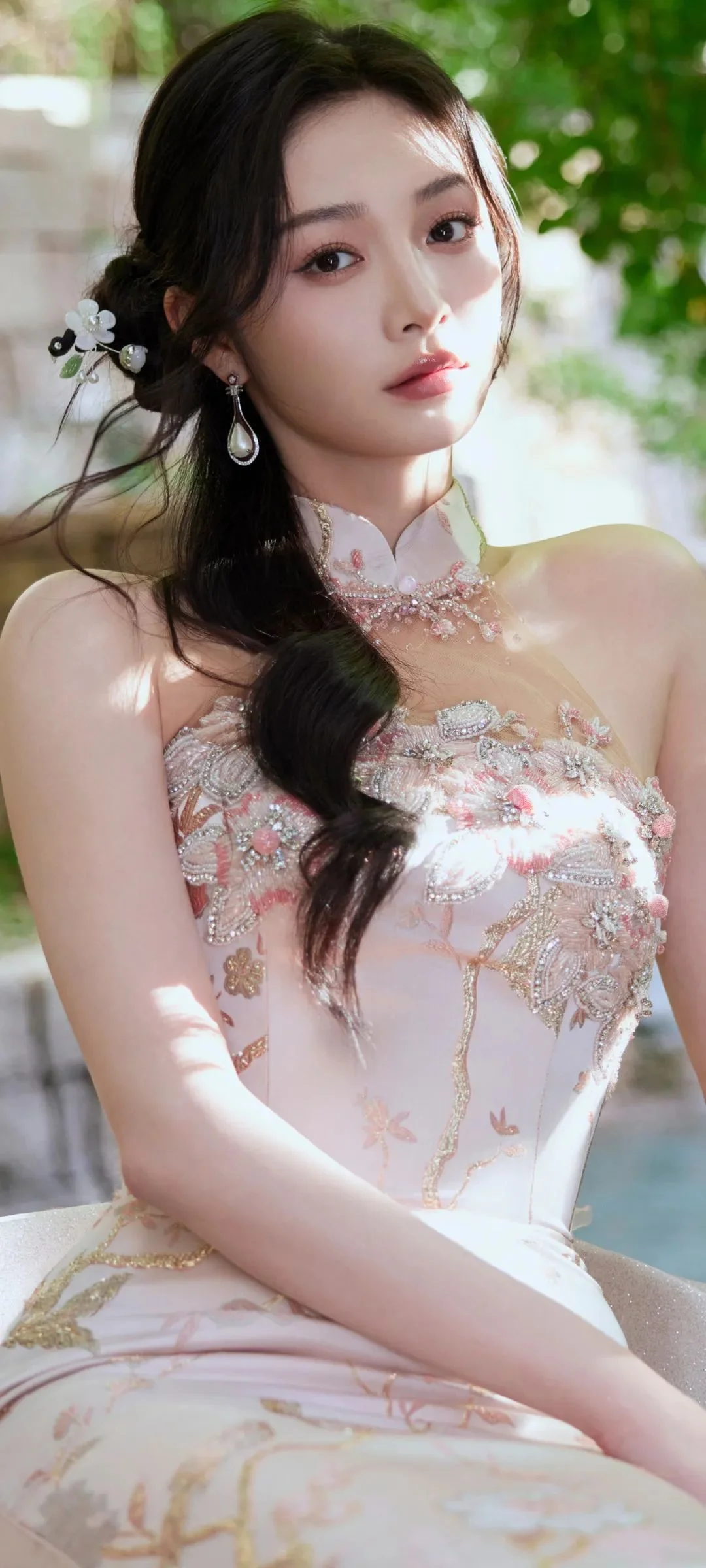 밝은 야외 햇살 아래에서 연한 전통풍 드레스를 입은 여성이 카메라를 바라보고 있다.
