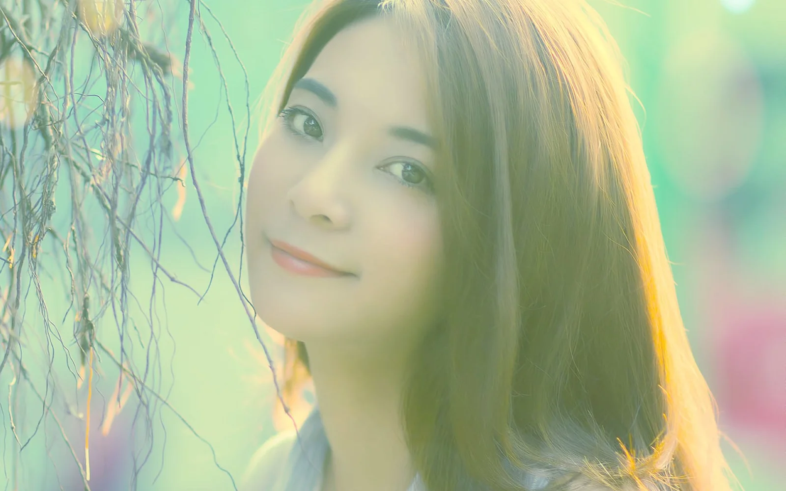 一位长发女性在柔和的绿色光影中靠近枝条微笑。