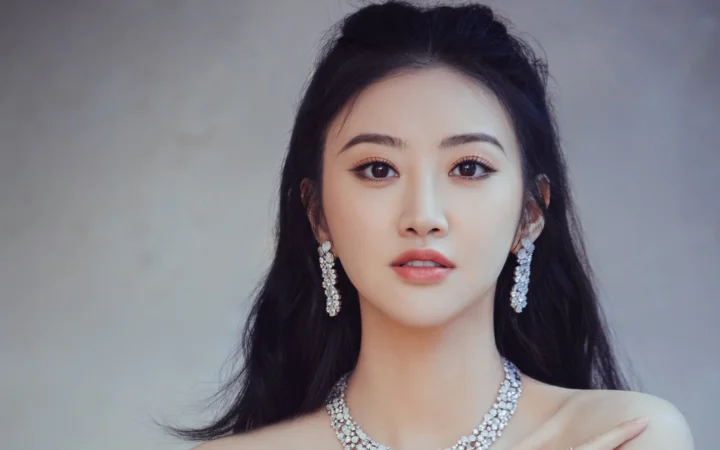 반짝이는 주얼리를 착용한 긴 머리 여성이 카메라를 바라보는 스튜디오 인물 사진입니다.