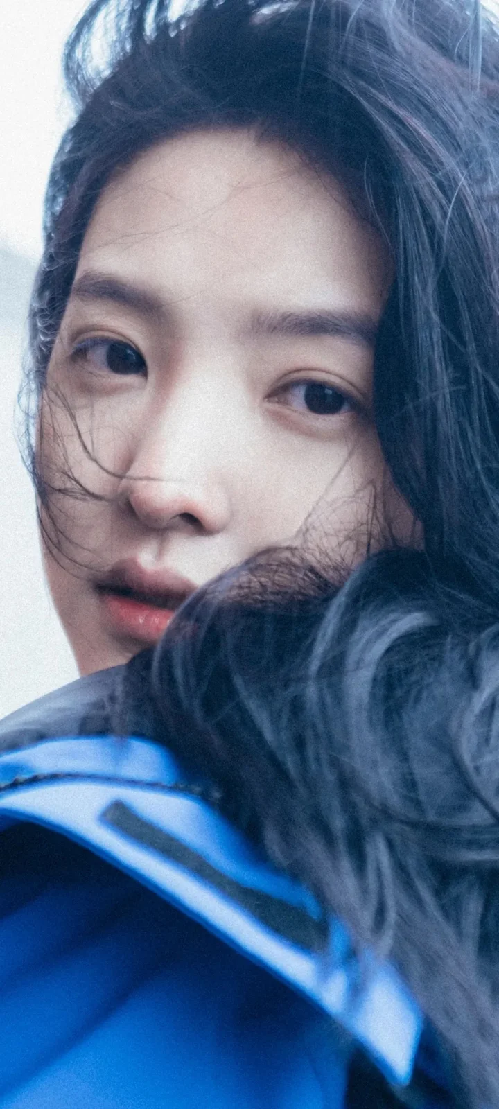 검은 머리 여성의 얼굴을 가까이 담은 인물 사진으로, 얼굴 일부가 전경의 어두운 머리카락과 파란 옷에 가려져 있습니다.