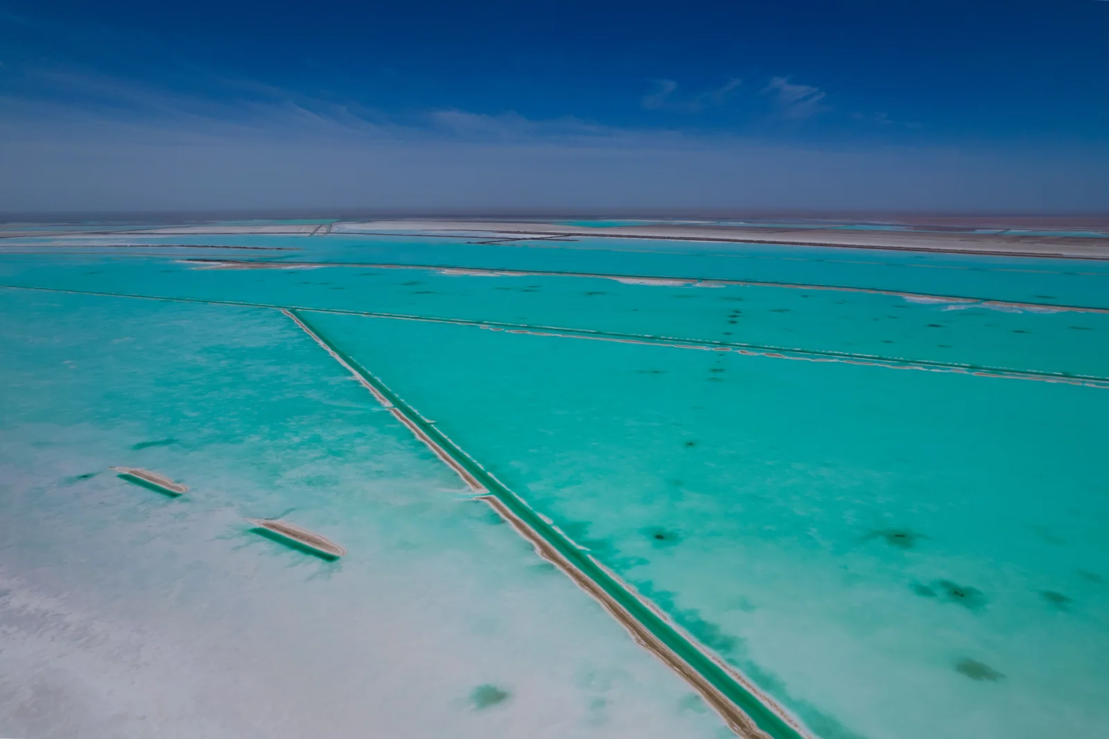 航拍视角展现了碧 turquoise 水面、浅色盐田分隔线和远处的水平线。