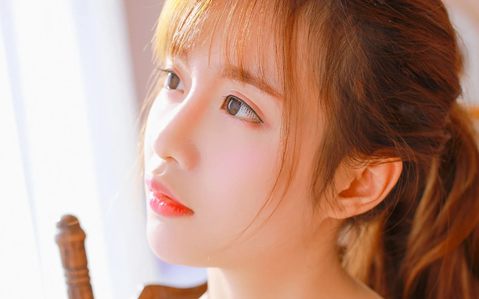 밝은 빛 속에서 적갈색 머리의 여성이 옆얼굴로 한쪽을 바라보는 클로즈업입니다.