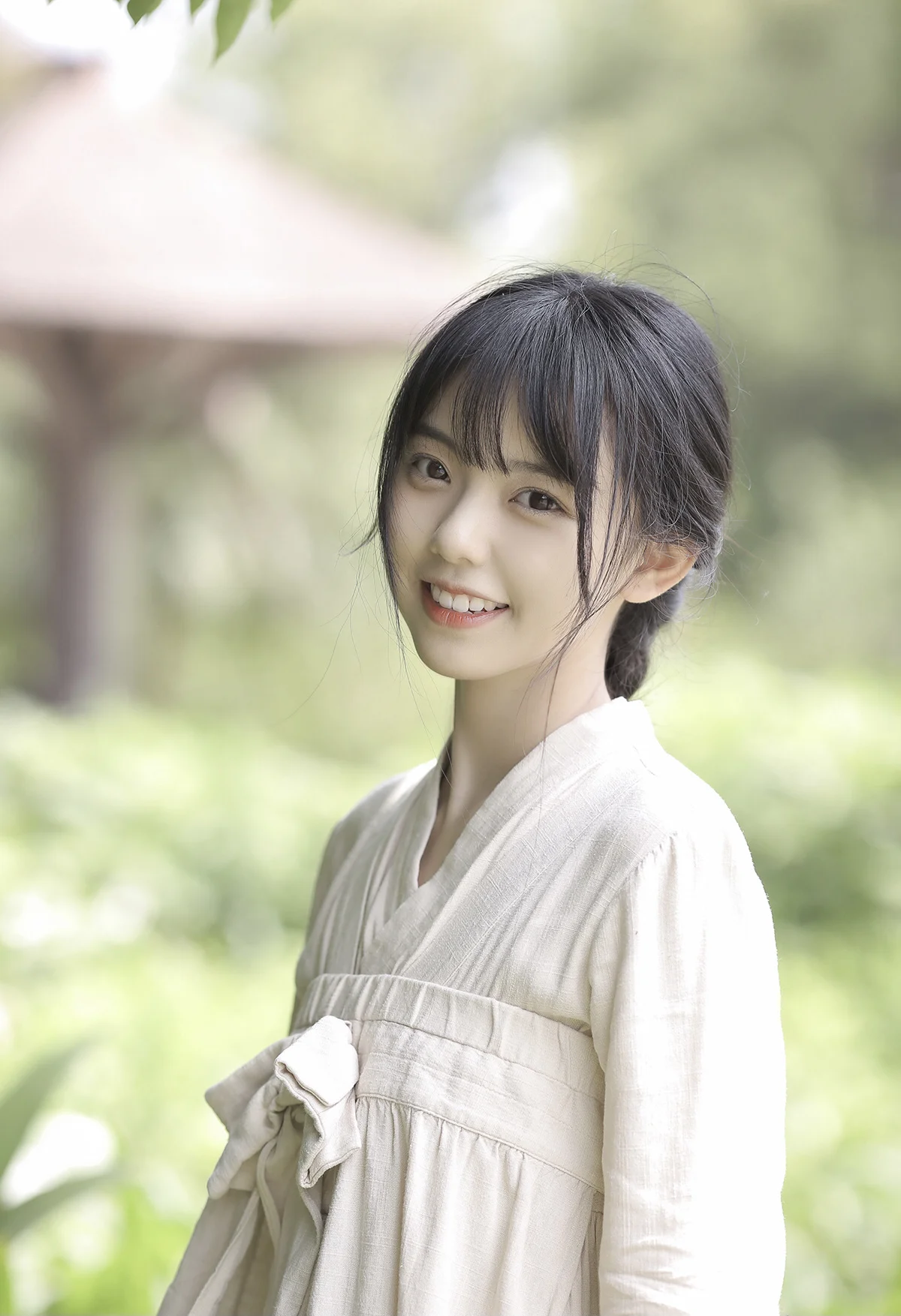 밝은 색 옷을 입은 여성이 푸른 야외에서 카메라를 바라보며 미소 짓고 있다.