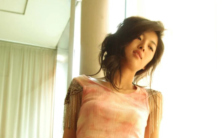 一名女性穿着粉色上衣站在室内窗边。