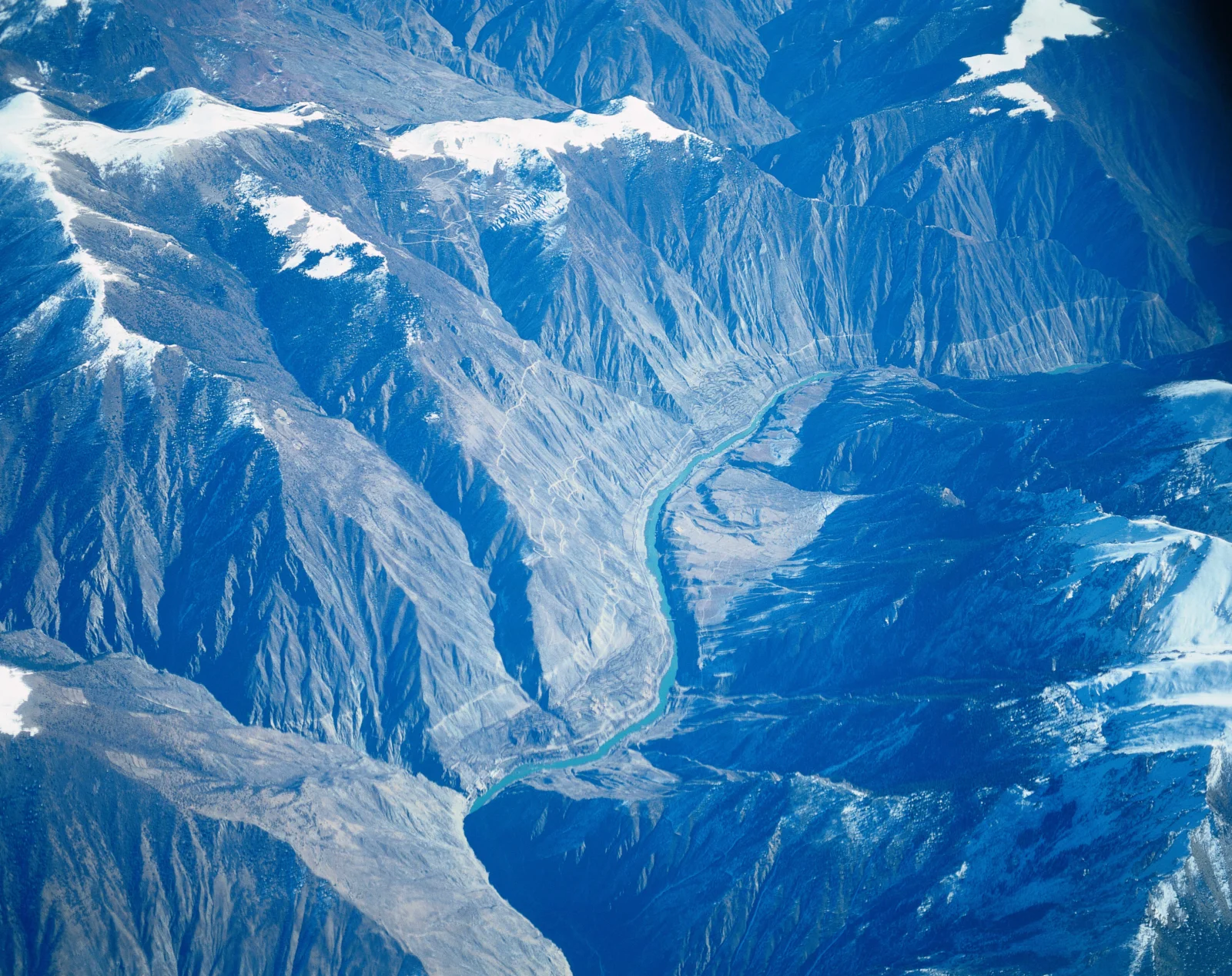 俯瞰视角展现了积雪山脉、深峻峡谷和蜿蜒河流。