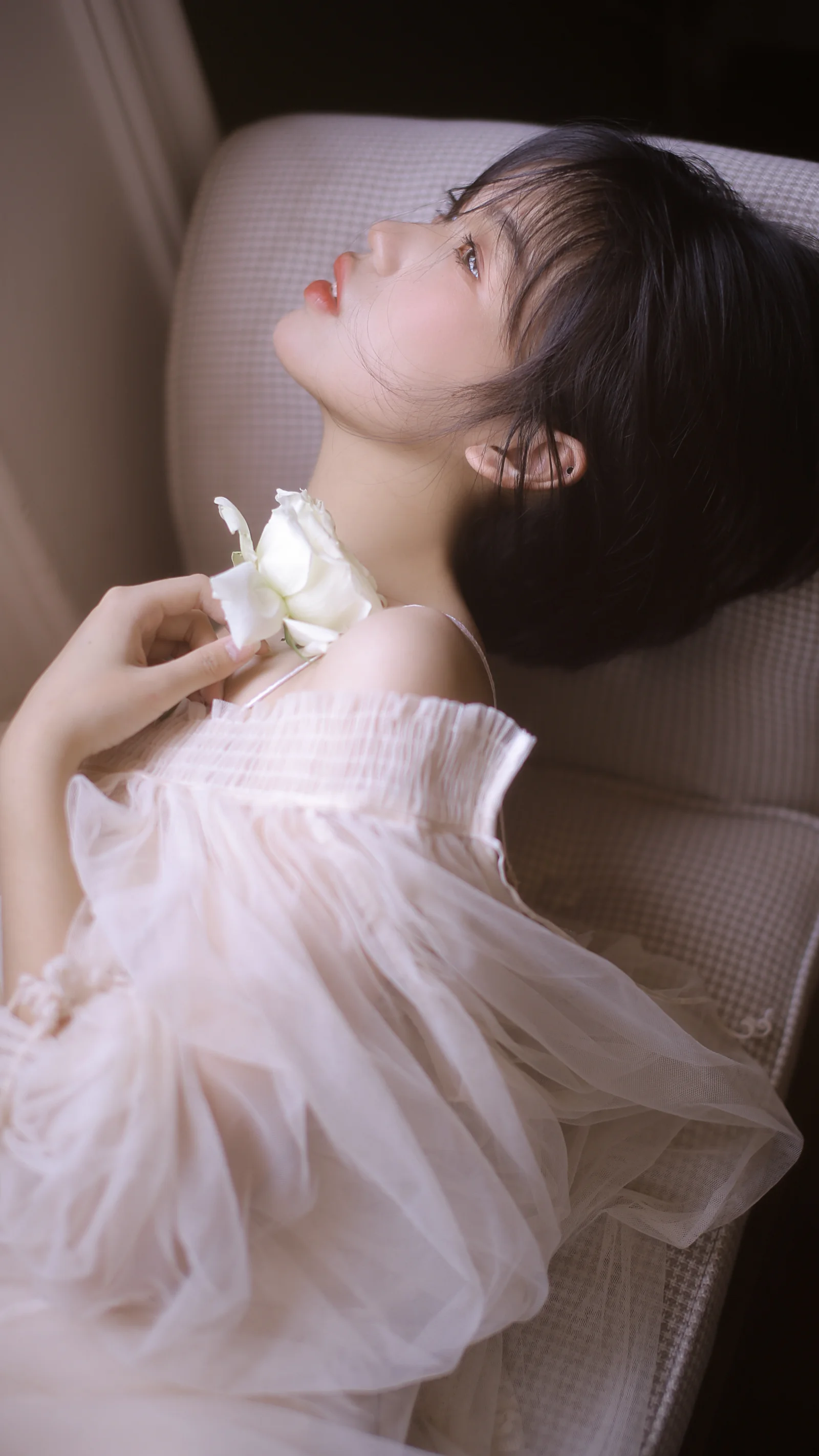 一名身穿白色薄纱裙的女性侧卧在椅子上，手持白色花朵。