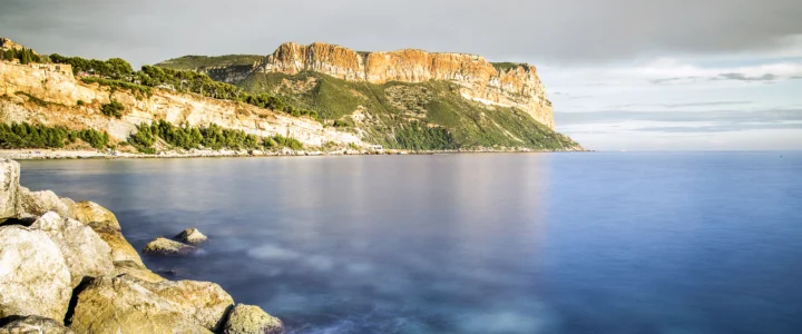 壮丽的山崖沿着宁静海岸延伸，前景是岩石海滩与平静的蓝色海面。