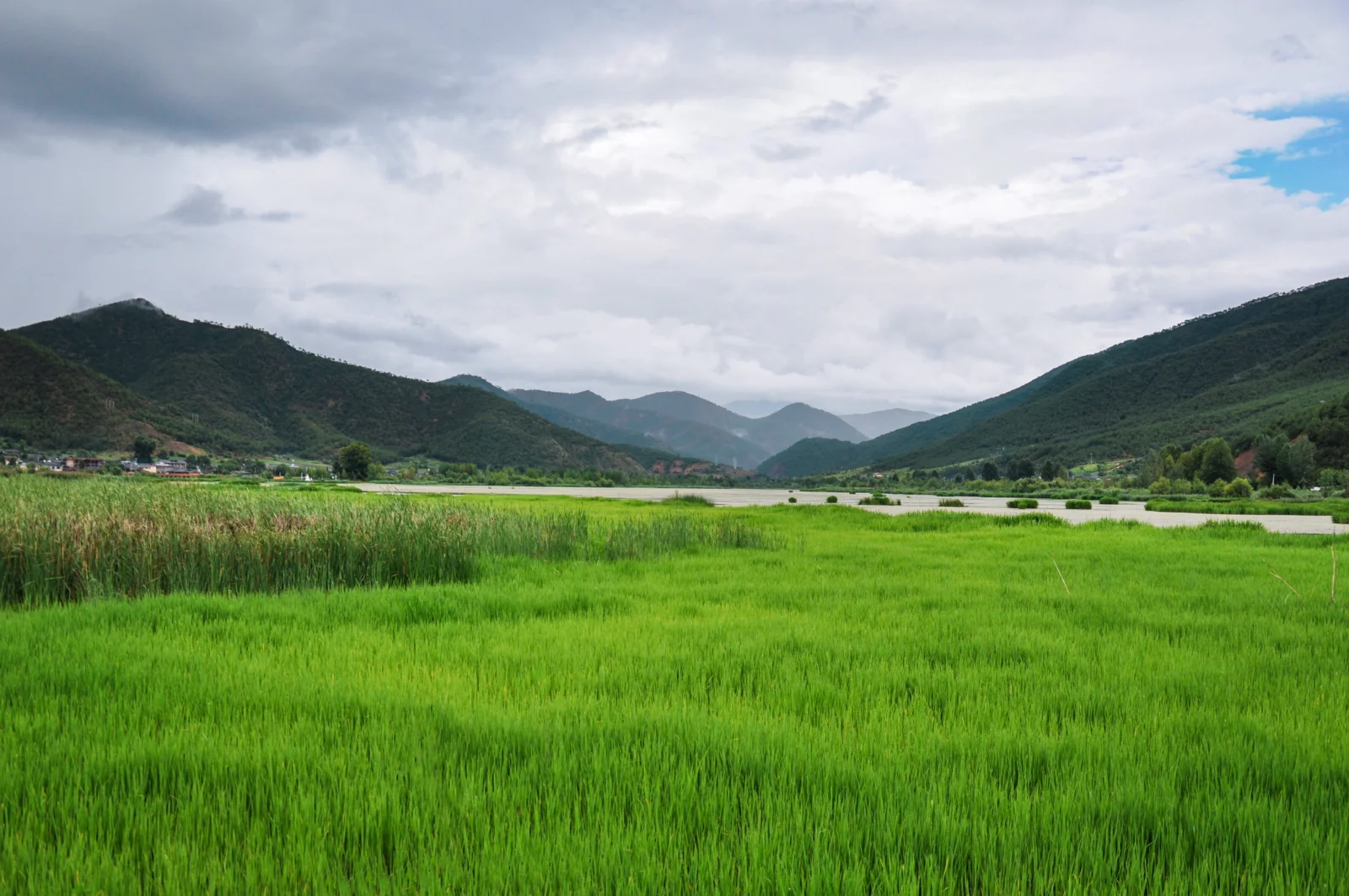 绿色草地延伸至山谷与湖面，远处群山在阴云天空下层叠展开。
