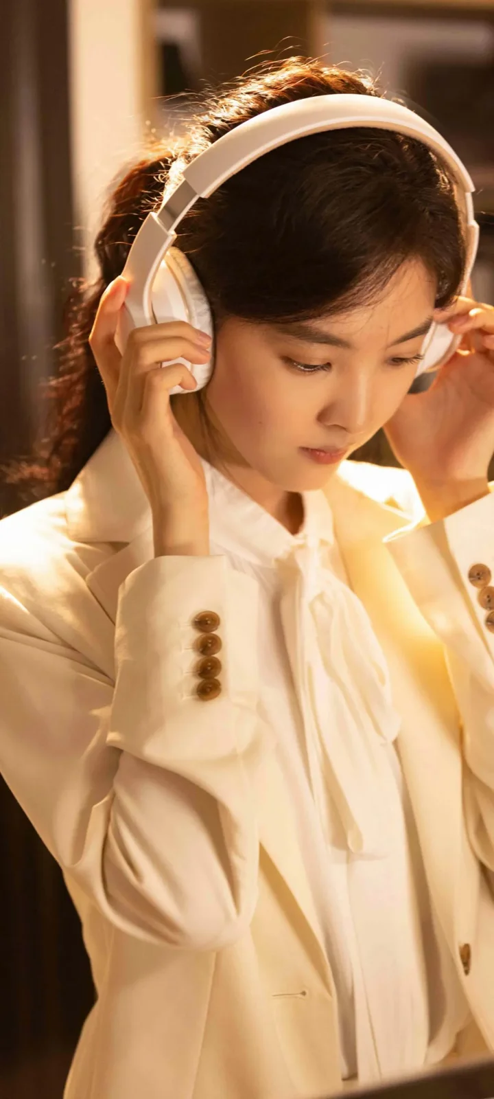 一名身穿白色外套的女性在温暖光线下佩戴白色耳机。