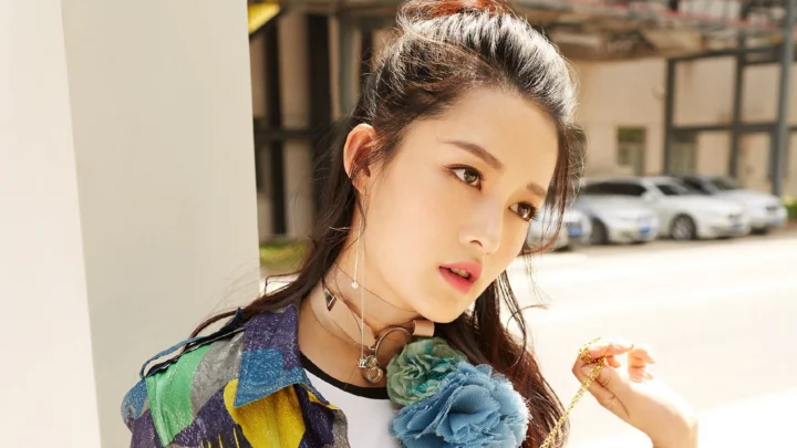 一名成年女性在户外阳光下佩戴蓝色花饰并穿着彩色服装。